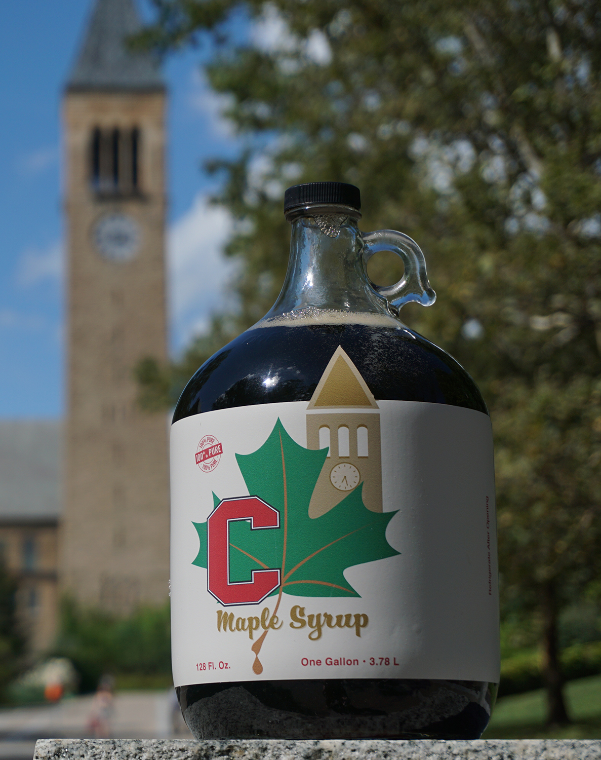 jug of maple syrup in front of Cornell clock tower